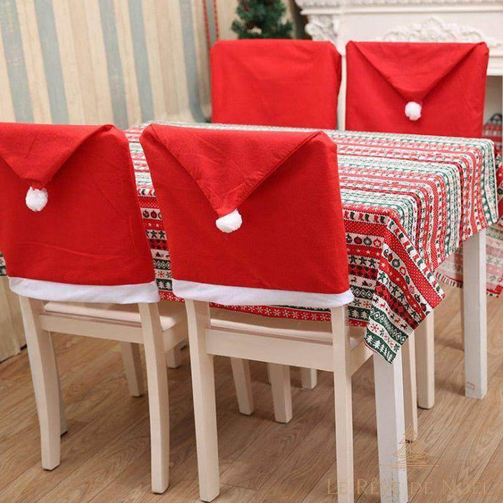 Housses de chaise bonnet de Noël rouges à pompon blanc, enfilées sur quatre chaises à table dressée