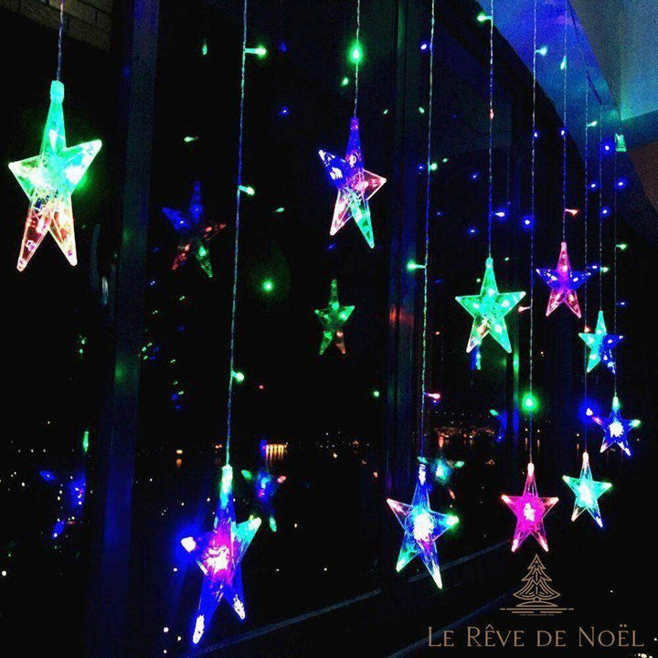 Guirlande lumineuse étoiles multicolores allumée la nuit devant une fenêtre, ville en arrière-plan