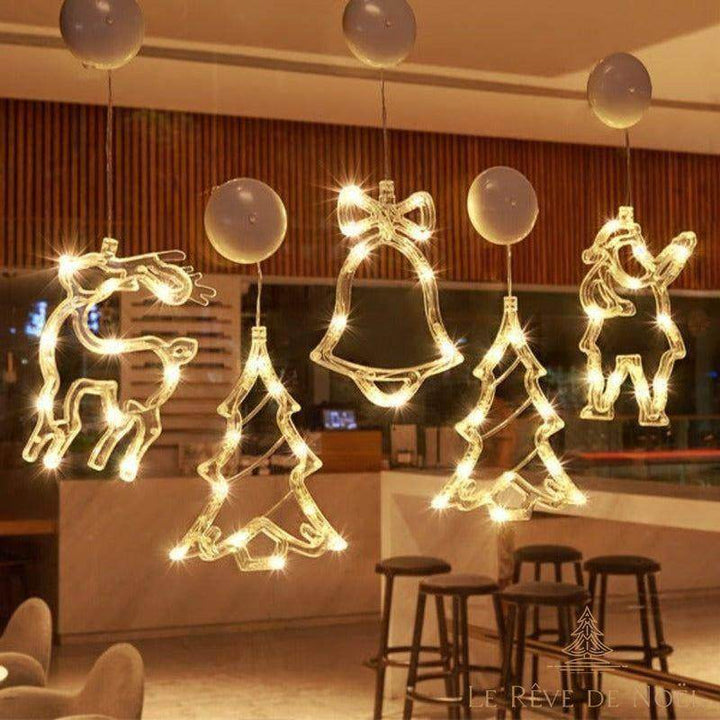 Guirlandes lumineuses cerf, sapins, cloche et Père Noël accrochées à une vitre de café le soir