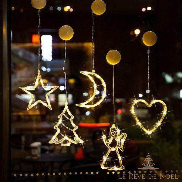 Guirlandes lumineuses en forme d'étoile, sapin, lune, ange et cœur accrochées à une vitre nocturne
