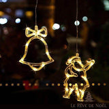 Néons allumés en forme de cloche et de Père Noël suspendus côte à côte, fond de bokeh nocturne