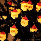 Gros plan sur des mini visages de Père Noël lumineux accrochés aux branches d'un sapin