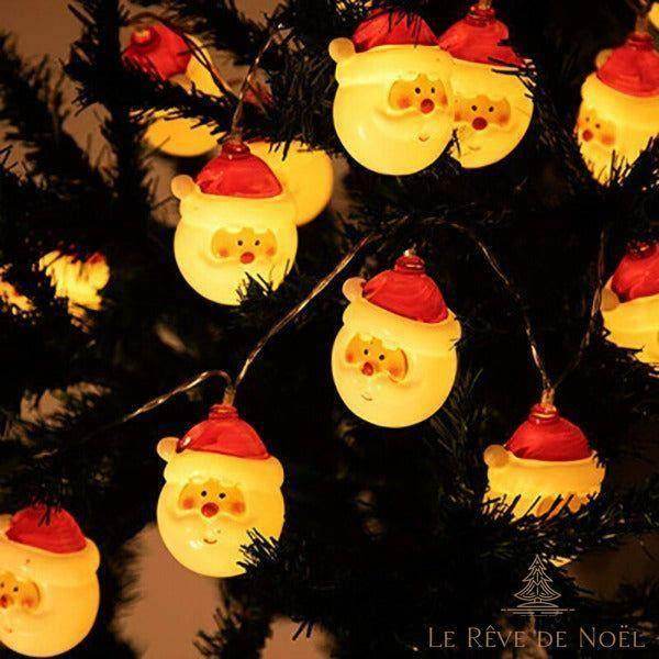 Gros plan sur des mini visages de Père Noël lumineux accrochés aux branches d'un sapin