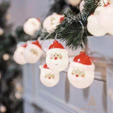 Guirlande lumineuse à petites têtes de Père Noël blanches et rouges accrochée sur une rampe décorée de sapin