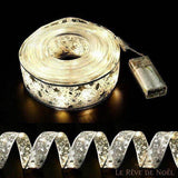 Bobine de ruban blanc argenté à LED allumées près de son boîtier à piles, ruban déroulé en bas
